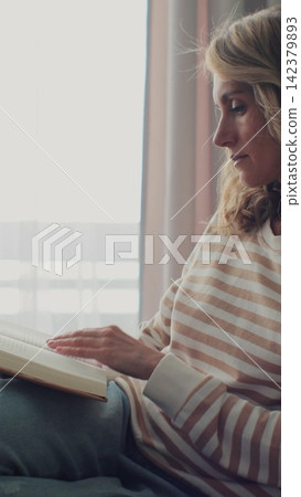 Vertical video. Woman reading book on sofa at home. Calm and comfortable. Vertical video. Woman reading book on sofa at home. Calm and comfortable. 142379893