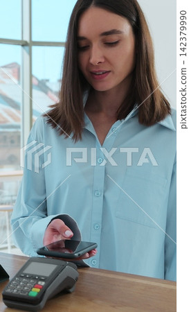 Vertical video. In the cafe barista man makes coffee for a woman customer which pays by contactless mobile phone to credit card system. Vertical video. In the cafe barista man makes coffee for a woman customer which pays by contactless mobile phone to credit card system. 142379990