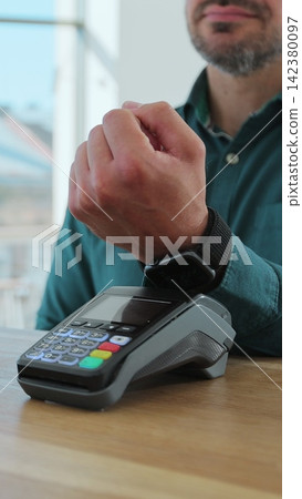 Vertical video. Man paying for coffee with nfc technology by smartwatch contactless on terminal in modern cafe. Non-cash payment concept. Vertical video. Man paying for coffee with nfc technology by smartwatch contactless on terminal in modern cafe. Non-cash payment concept. 142380097