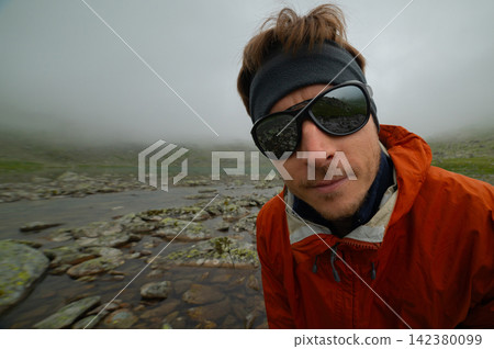 Hiker in orange jacket near mountain lake Hiker in orange jacket near mountain lake 142380099
