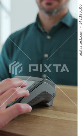 Vertical video. Man paying for coffee with nfc technology by smartwatch contactless on terminal in modern cafe. Non-cash payment concept. Vertical video. Man paying for coffee with nfc technology by smartwatch contactless on terminal in modern cafe. Non-cash payment concept. 142380100