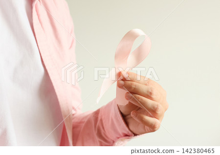 Close-up of a woman wearing a pink shirt holding a pink ribbon symbolizing breast cancer awareness. Health, medicine, and support concept. Breast Cancer Awareness Month Close-up of a woman wearing a pink shirt holding a pink ribbon symbolizing breast cancer awareness. Health, medicine, and support concept. Breast Cancer Awareness Month 142380465