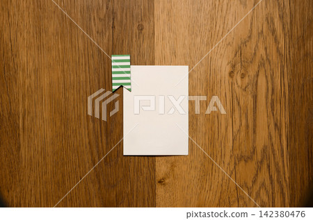Top-down view of a blank white card with a green striped paper clip on a textured wooden table background. Mockup, design, and note concept Top-down view of a blank white card with a green striped paper clip on a textured wooden table background. Mockup, design, and note concept 142380476