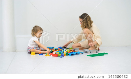 Sisters sitting on the floor sorting through a large pile of colorful plastic construction blocks. Educational bonding concept Sisters sitting on the floor sorting through a large pile of colorful plastic construction blocks. Educational bonding concept 142380482