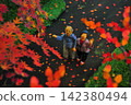 An elderly couple strolling along a path lined with autumn leaves. 142380494