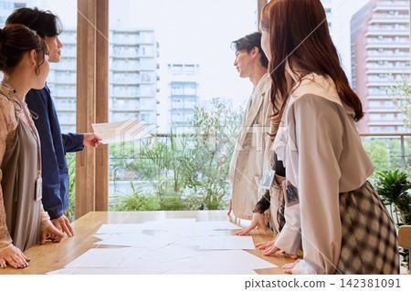 年輕的商務人士在辦公室裡一邊開會一邊查看文件。 年輕的商務人士在辦公室裡一邊開會一邊查看文件。 142381091
