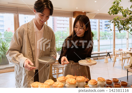 A smiling young couple chooses a pie dish at a cafe buffet. A smiling young couple chooses a pie dish at a cafe buffet. 142381116