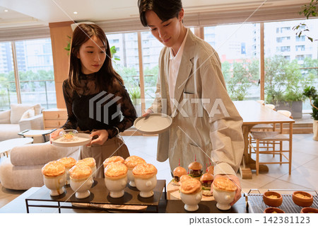 一對年輕夫婦在自助餐檯上挑選糕點湯和其他菜餚。 一對年輕夫婦在自助餐檯上挑選糕點湯和其他菜餚。 142381123