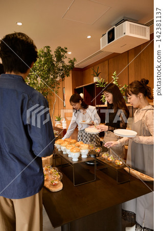 Young women serving buffet food at a home party. Young women serving buffet food at a home party. 142381137