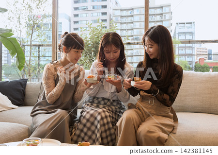 Three young women enjoying sweets at a stylish cafe. Three young women enjoying sweets at a stylish cafe. 142381145