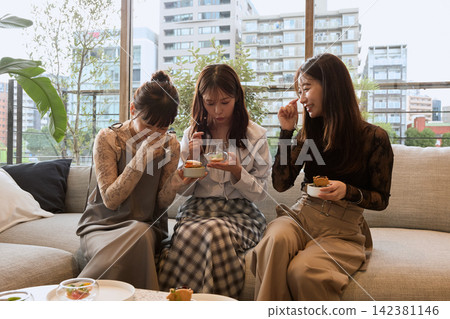 三個年輕女子在咖啡館的沙發上聊天吃甜點。 142381146