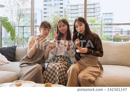 三個年輕女子在咖啡館的沙發上享用甜點。 三個年輕女子在咖啡館的沙發上享用甜點。 142381147