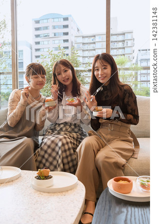 三位年輕女子在時尚咖啡館享用甜點。 142381148