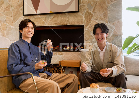 兩個年輕男子在有壁爐的休息室裡享用甜點。 兩個年輕男子在有壁爐的休息室裡享用甜點。 142381150