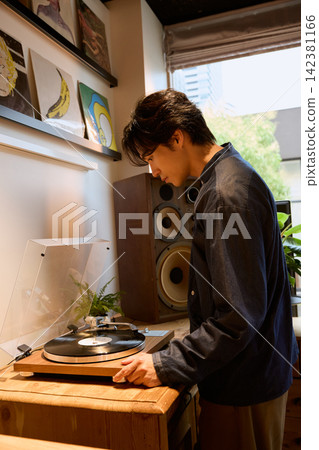 A young man sets a record on his record player at home. A young man sets a record on his record player at home. 142381166