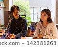 一對年輕情侶在咖啡館愉快地交談，手裡拿著酒杯。 142381263