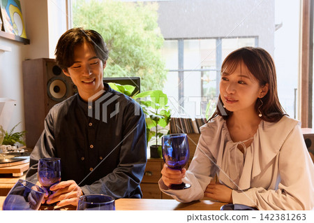 一對年輕情侶在咖啡館愉快地交談，手裡拿著酒杯。 142381263