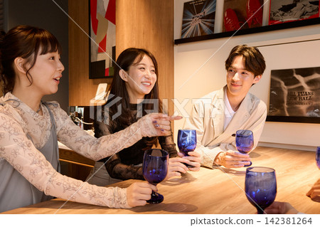 三位年輕男女手持藍色酒杯，在酒吧愉快地交談。 142381264