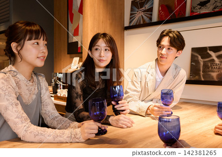 三位年輕男女在酒吧愉快地交談，每人手裡都拿著一杯酒。 142381265