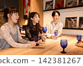 三位年輕男女手持酒杯，在酒吧愉快地交談著。 142381267