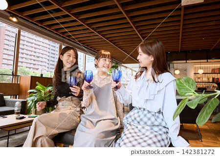 三位年輕女子在一家時尚咖啡館裡舉杯祝酒。 142381272