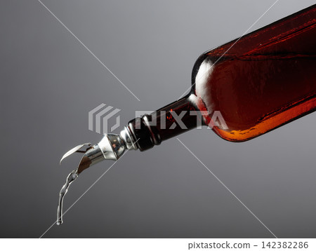 Antique dark brown glass bottle with vintage pourer on a gray background. 142382286