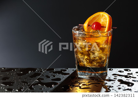 Old fashioned cocktail in a sweating glass on a wet black table. Old fashioned cocktail in a sweating glass on a wet black table. 142382311