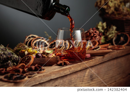 Herbal balm or tincture is poured from a vintage bottle into a glass. Herbal balm or tincture is poured from a vintage bottle into a glass. 142382404