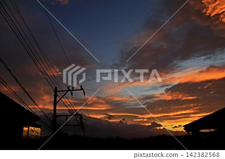 The sunset sky stretches out beyond the silhouettes of power lines and cityscapes. The sunset sky stretches out beyond the silhouettes of power lines and cityscapes. 142382568