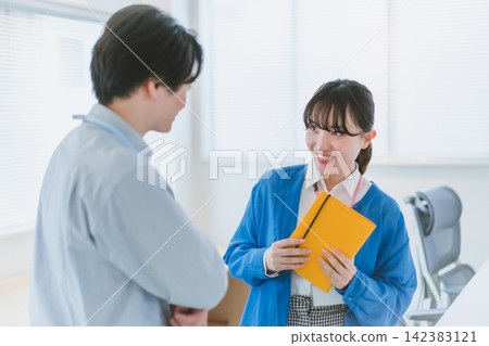 辦公室戀情:一位女員工拿著筆記本,面帶微笑地與一位男性同事交談。 辦公室戀情:一位女員工拿著筆記本,面帶微笑地與一位男性同事交談。 142383121
