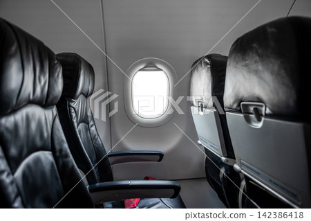 Airplane cabin interior, empty comfortable passenger seats in economy class with portholes. Airplane cabin interior, empty comfortable passenger seats in economy class with portholes. 142386418