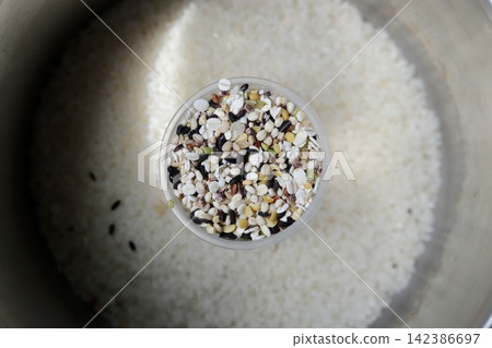 White rice in a stainless steel pot before cooking, and sixteen-grain rice in a measuring cup. White rice in a stainless steel pot before cooking, and sixteen-grain rice in a measuring cup. 142386697