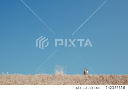 A young woman standing in a field with a blue sky. A young woman standing in a field with a blue sky. 142386836