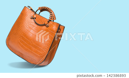 Classic tan brown crocodile pattern leather handbag on light blue background with copy space. Modern womens tote bag side view Classic tan brown crocodile pattern leather handbag on light blue background with copy space. Modern womens tote bag side view 142386893