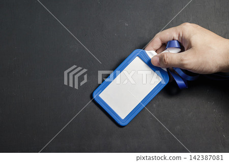 A close-up of a hand holding a blank blue plastic identity badge with a blue lanyard ribbon over a dark background, perfect for security and access mockups. High Quality Photo A close-up of a hand holding a blank blue plastic identity badge with a blue lanyard ribbon over a dark background, perfect for security and access mockups. High Quality Photo 142387081
