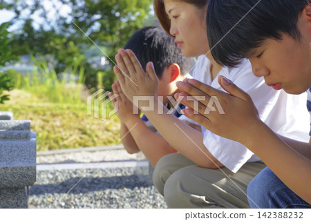 A mother and her children praying at the grave. 142388232