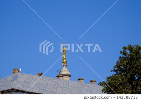 Golden Religious Statue Rising Above Historic Rooftop Against Clear Blue Sky in Kamianets Podilskyi Ukraine Golden Religious Statue Rising Above Historic Rooftop Against Clear Blue Sky in Kamianets Podilskyi Ukraine 142388718