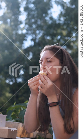 woman eating cake outdoors in a relaxed and happy setting with sunglasses on head and smartwatch, side view close-up with brown hair and wooden surface, brown and white colors, food and lfe. woman eating cake outdoors in a relaxed and happy setting with sunglasses on head and smartwatch, side view close-up with brown hair and wooden surface, brown and white colors, food and lfe. 142389016
