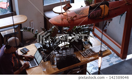 man working on laptop in focused and relaxed cafe setting with wooden furniture and smartphone nearby, top-down view, work from home, freelance work, remote work, brown, green, white, black. man working on laptop in focused and relaxed cafe setting with wooden furniture and smartphone nearby, top-down view, work from home, freelance work, remote work, brown, green, white, black. 142389046