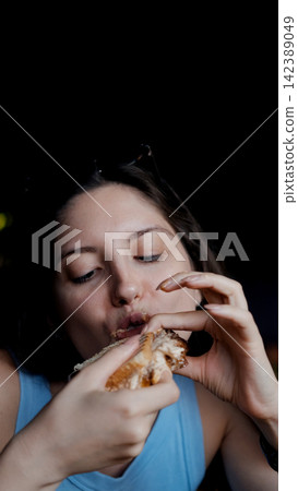 woman eating sandwich in dark setting with contentment close-up hand bread filling food lifestyle blue brown commercial natural light clean copy space editorial educational visual story web. woman eating sandwich in dark setting with contentment close-up hand bread filling food lifestyle blue brown commercial natural light clean copy space editorial educational visual story web. 142389049