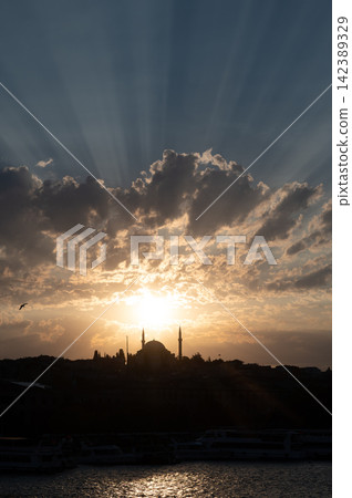 Istanbul,turkey,august 2, 2025. Istanbul city skyline at sunset, featuring a historical mosque and minarets silhouetted against a dramatic sky with sunbeams over the bosphorus 142389329
