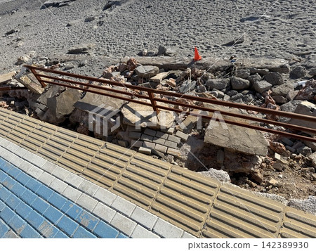 Broken walkway with damaged railing and rubble near sandy beach under bright sunlight Broken walkway with damaged railing and rubble near sandy beach under bright sunlight 142389930
