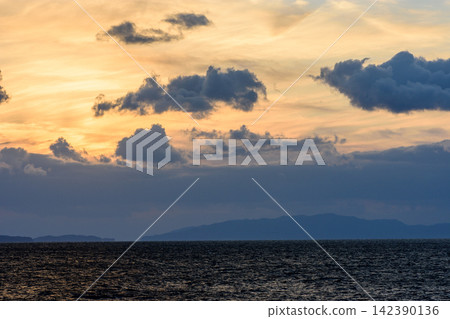 A tranquil sunset over a vast body of water, dominated by dynamic clouds and reflected light A tranquil sunset over a vast body of water, dominated by dynamic clouds and reflected light 142390136