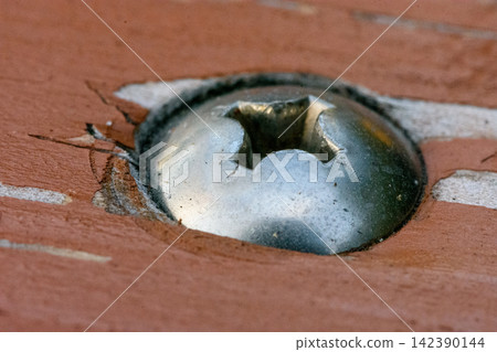 A severely damaged metallic screw embedded in reddish-brown wood with wear and tear signs A severely damaged metallic screw embedded in reddish-brown wood with wear and tear signs 142390144