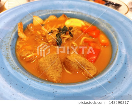 Rich and spicy curry noodle soup served in a blue bowl with hard-boiled egg and tofu 142390217