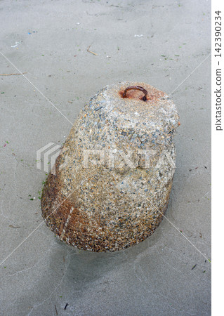 A weathered conical stone resting on a wet sand beach, with rusted metal embedded at its top A weathered conical stone resting on a wet sand beach, with rusted metal embedded at its top 142390234