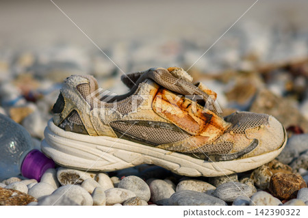 A severely worn and dirty athletic shoe resting on pebbles with rusted midsole and upper fabric A severely worn and dirty athletic shoe resting on pebbles with rusted midsole and upper fabric 142390322