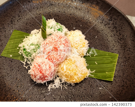 Traditional Indonesian Kue Klepon sweet green glutinous rice balls filled with molten palm sugar and coated in grated coconut on a banana leaf plate Traditional Indonesian Kue Klepon sweet green glutinous rice balls filled with molten palm sugar and coated in grated coconut on a banana leaf plate 142390373