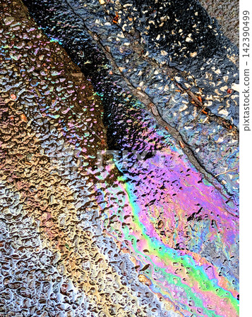 A leaked Car Oil Petrol in The Rain on a Tarmac Road Metallic Rainbow Gasoline A leaked Car Oil Petrol in The Rain on a Tarmac Road Metallic Rainbow Gasoline 142390499
