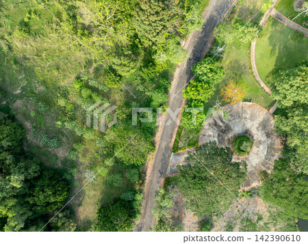 Aerial drone view of landscaped circular plaza and garden paths in lush wellness retreat resort, surrounded by tropical trees and quiet roads. Eco travel and relaxation. Peaceful resort planning. Aerial drone view of landscaped circular plaza and garden paths in lush wellness retreat resort, surrounded by tropical trees and quiet roads. Eco travel and relaxation. Peaceful resort planning. 142390610
